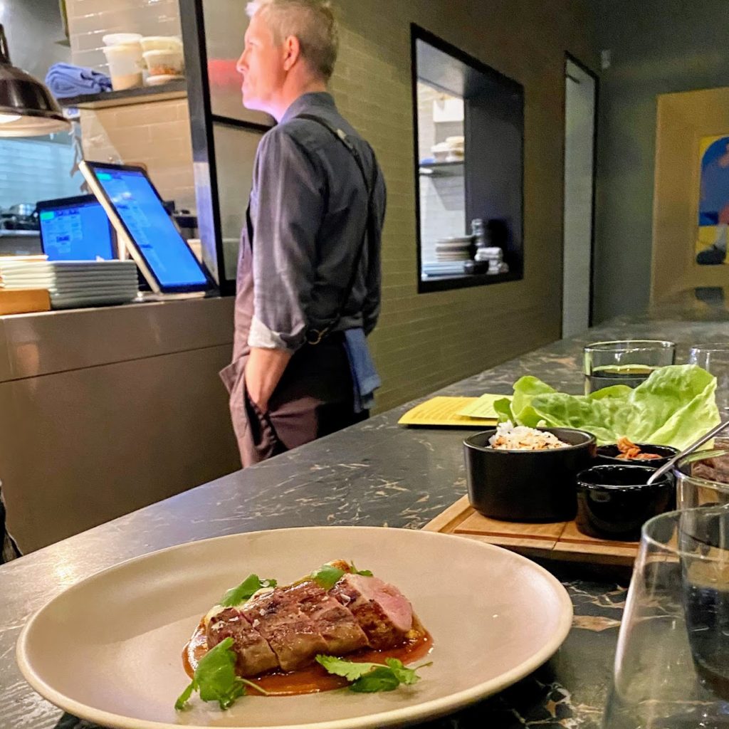 Wood-grilled pork tenderloin with smoked peanut mole and knob onions; wood-grilled prime beef short rib ssam with butter lettuce, pickled daikon, rice, and spicy ssamjang (plus a cameo from chef Andrew Zimmerman)